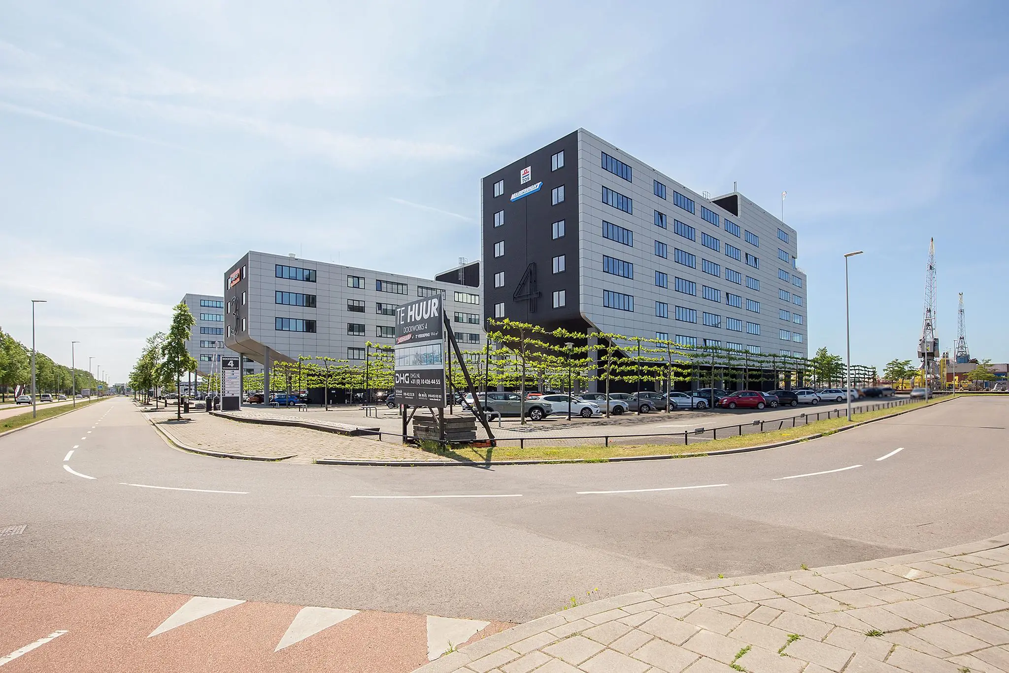 Kantoorcomplex aan de Waalhaven Oostzijde met parkeerterrein, verhuurbord en zicht op havenkranen op de achtergrond.
